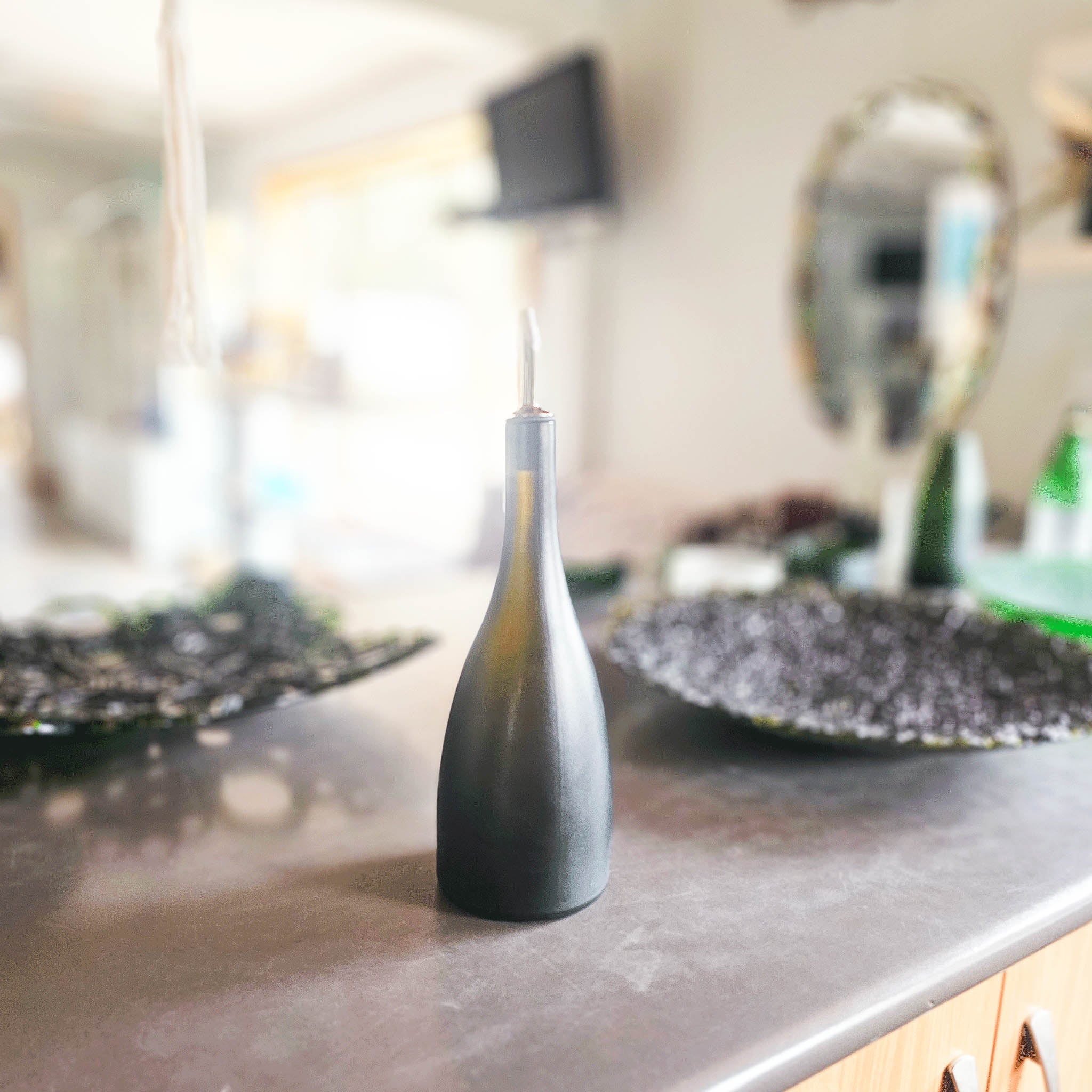 • Image of the Prestige Glass Oil Pourer This unique and luxurious accessory, born from upcycled champagne bottles, elevates your kitchen with its one-of-a-kind matte sateen finish and heat-altered shape.