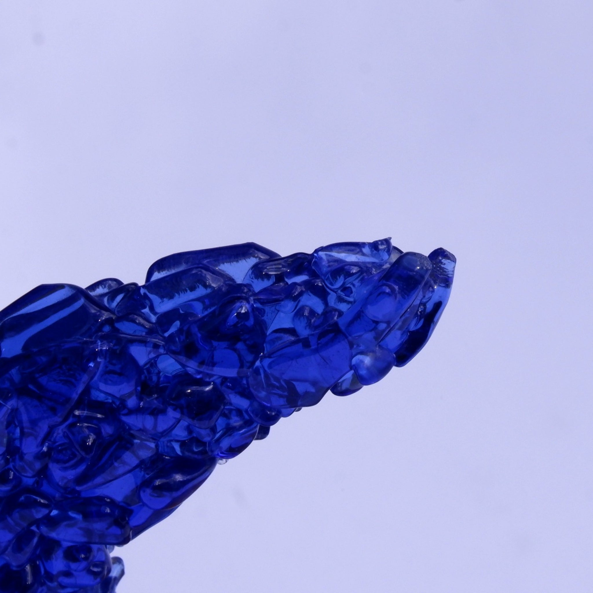 A close-up of the whale tail fluke, the fused fragments of the translucent deep blue glass against a cool pale lavender background.