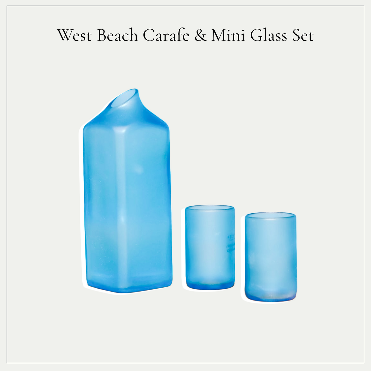 West Beach Carafe & Mini Glass Set featuring a translucent sapphire blue glass carafe and two matching mini tumblers, shown against a light gray background with black text at the top.