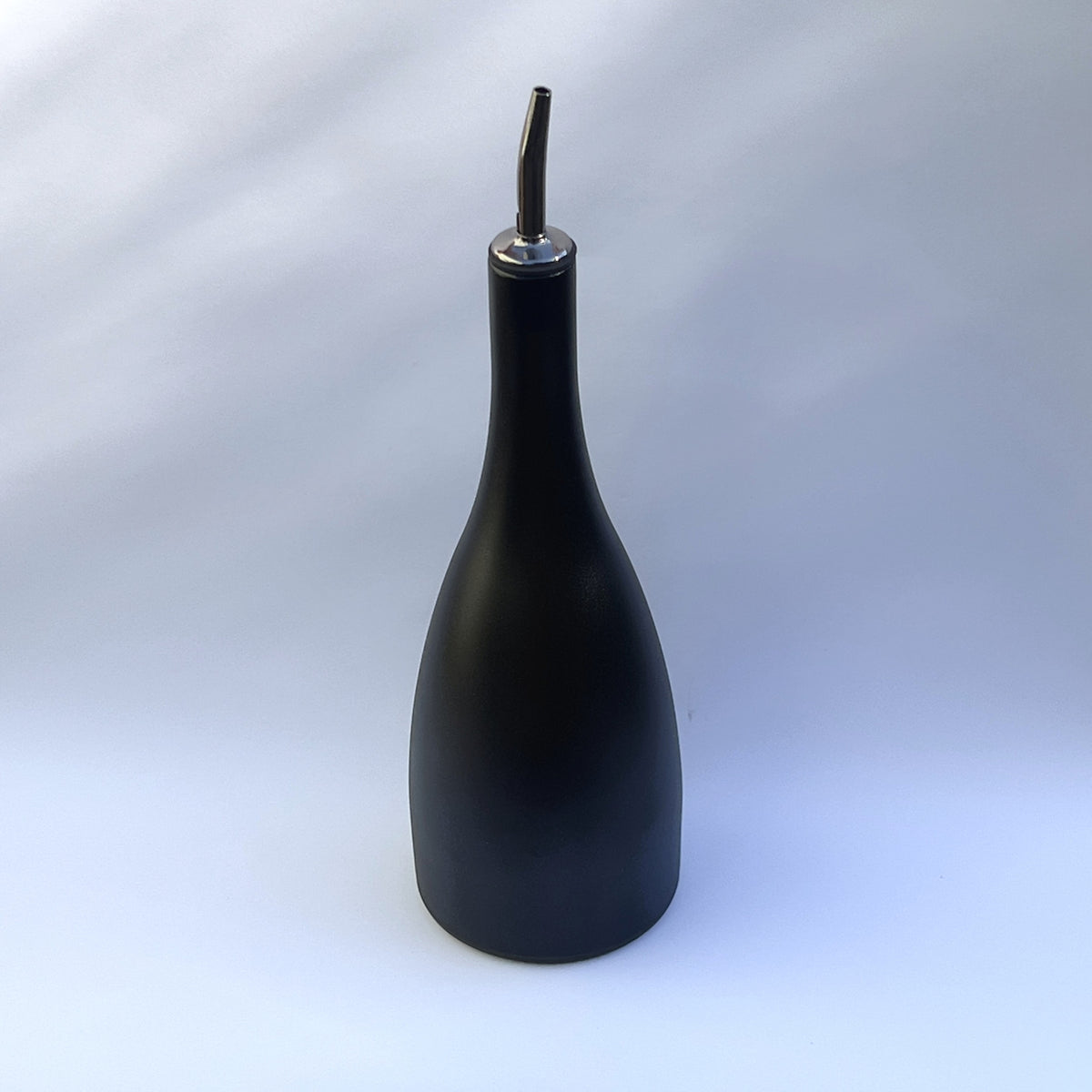 A matte black bottle-shaped oil dispenser with a metallic silver pour spout, set against a light gray studio background.