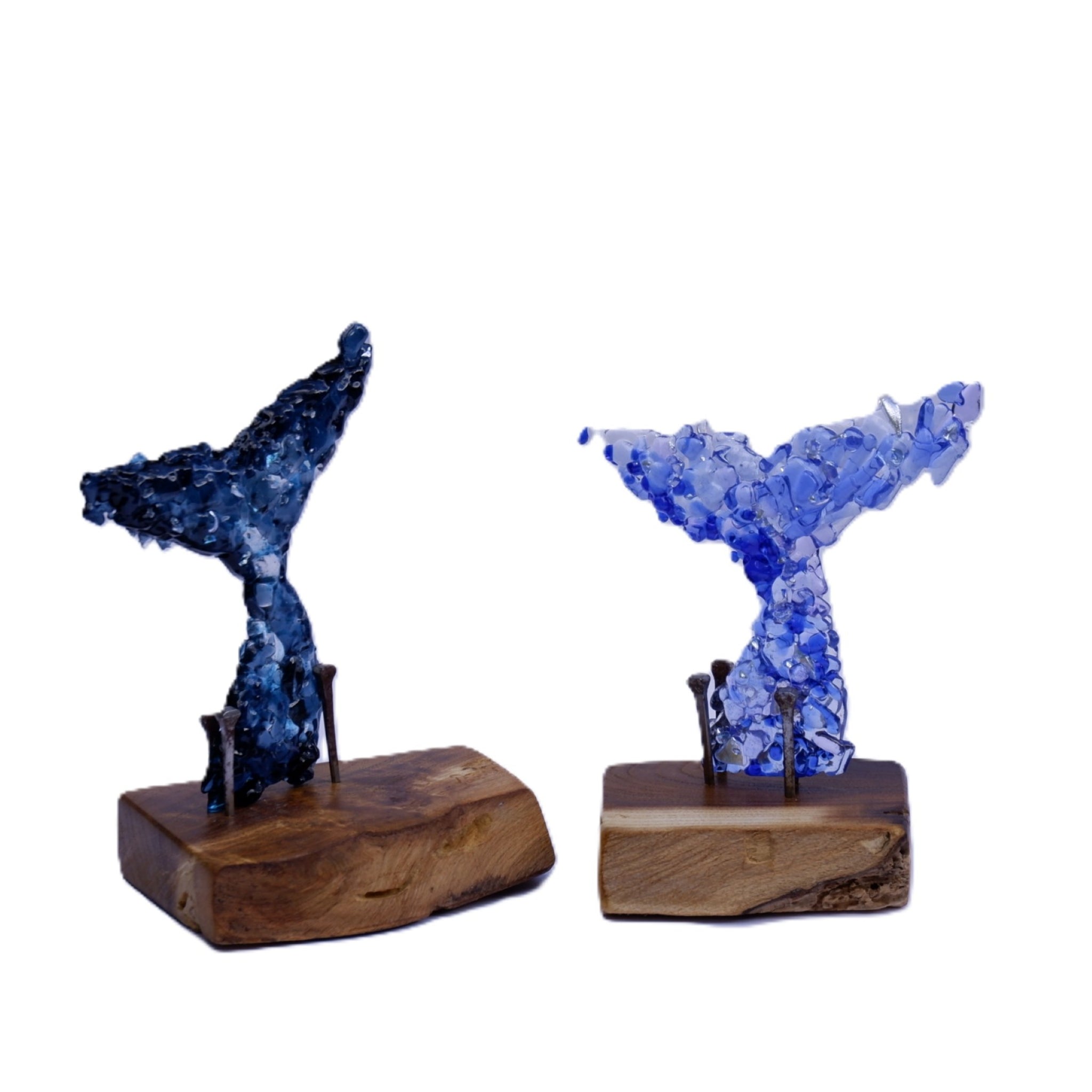 Two baby dichroic and art glass whale tail sculptures on natural sanded and oiled wooden bases, one in dark blue and one in light blue, displayed against a solid white background.