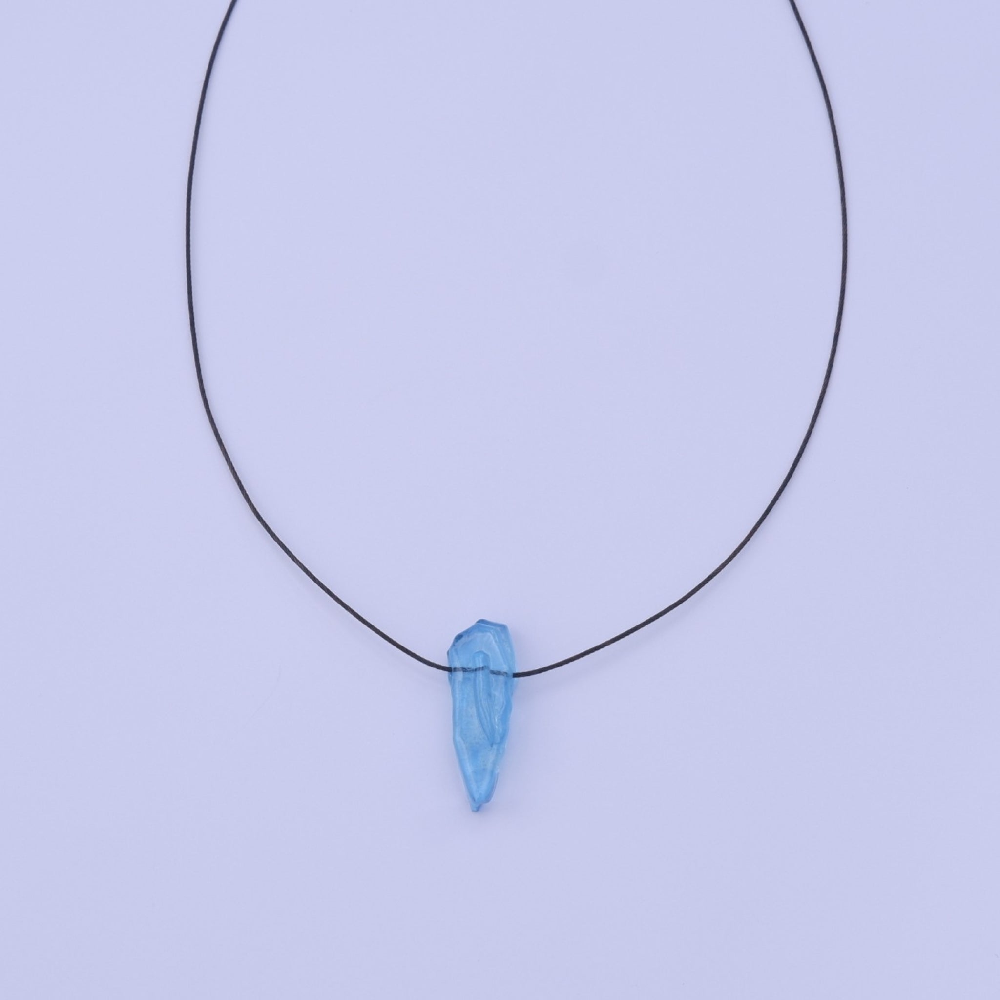 A delicate black stainless steel thread necklace featuring a single polished light blue teardrop styled glass pendant, displayed against a solid light colouredbackground.