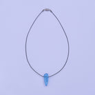 A delicate black stainless steel thread necklace featuring a single light blue teardrop styled glass pendant, displayed against a solid light coloured background.