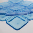 Close-up of translucent sapphire blue square glass bowl with reflection from a mirrored surface.