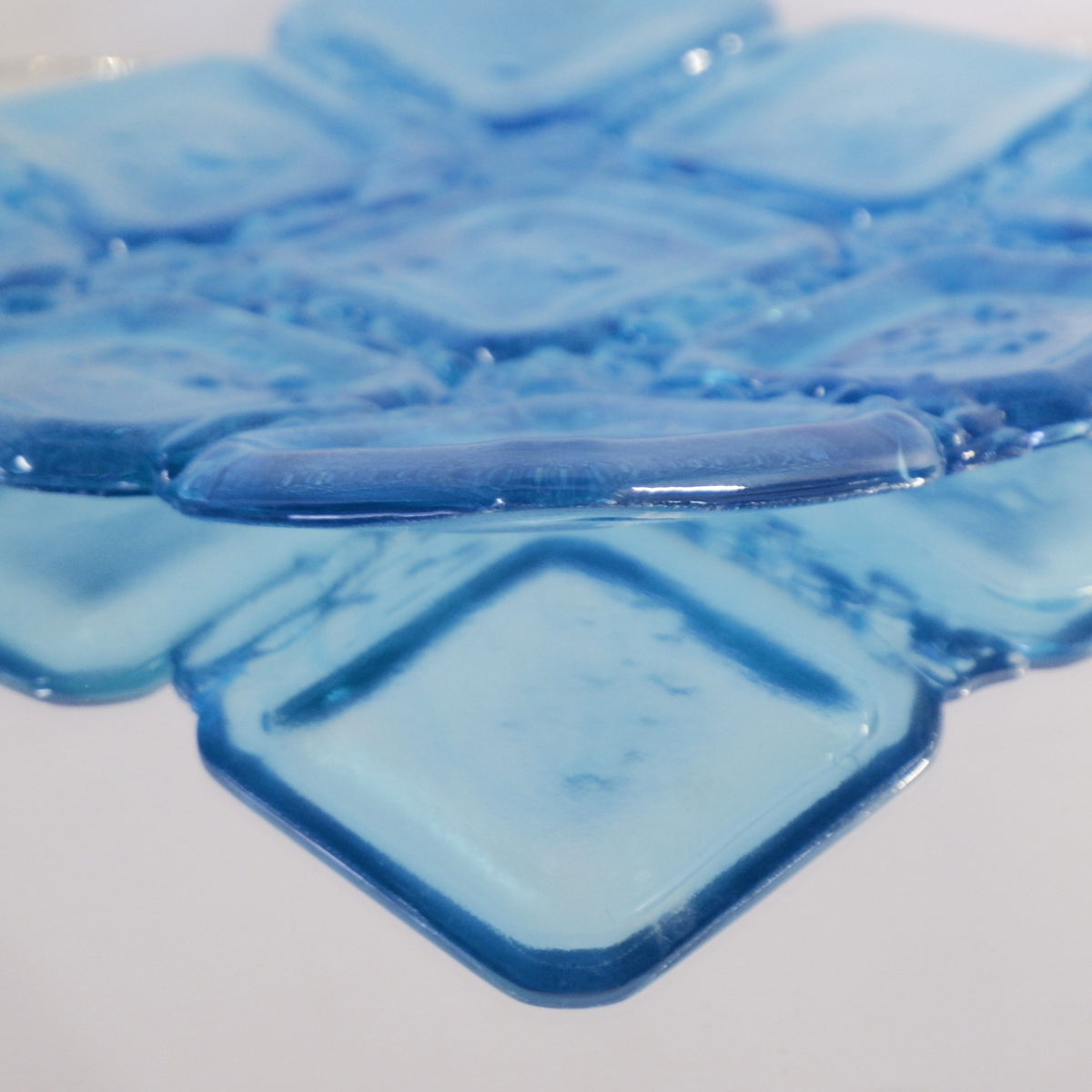 Close-up of translucent sapphire blue square glass bowl with reflection from a mirrored surface.