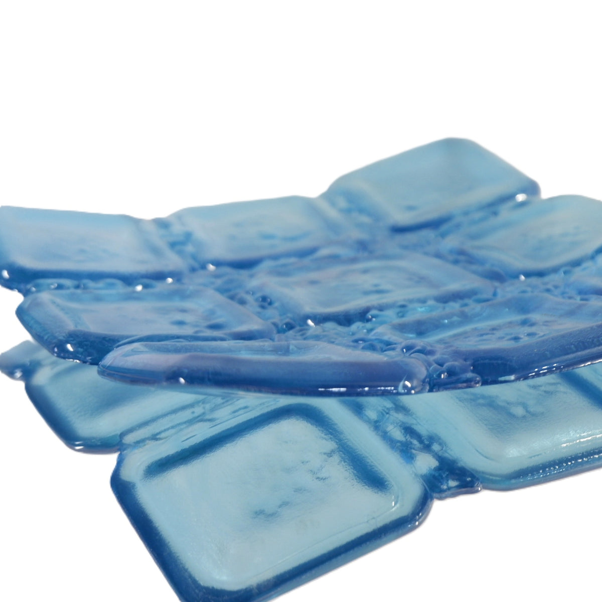 A sapphire blue translucent square glass bowl, arranged in a mirror with a white background.