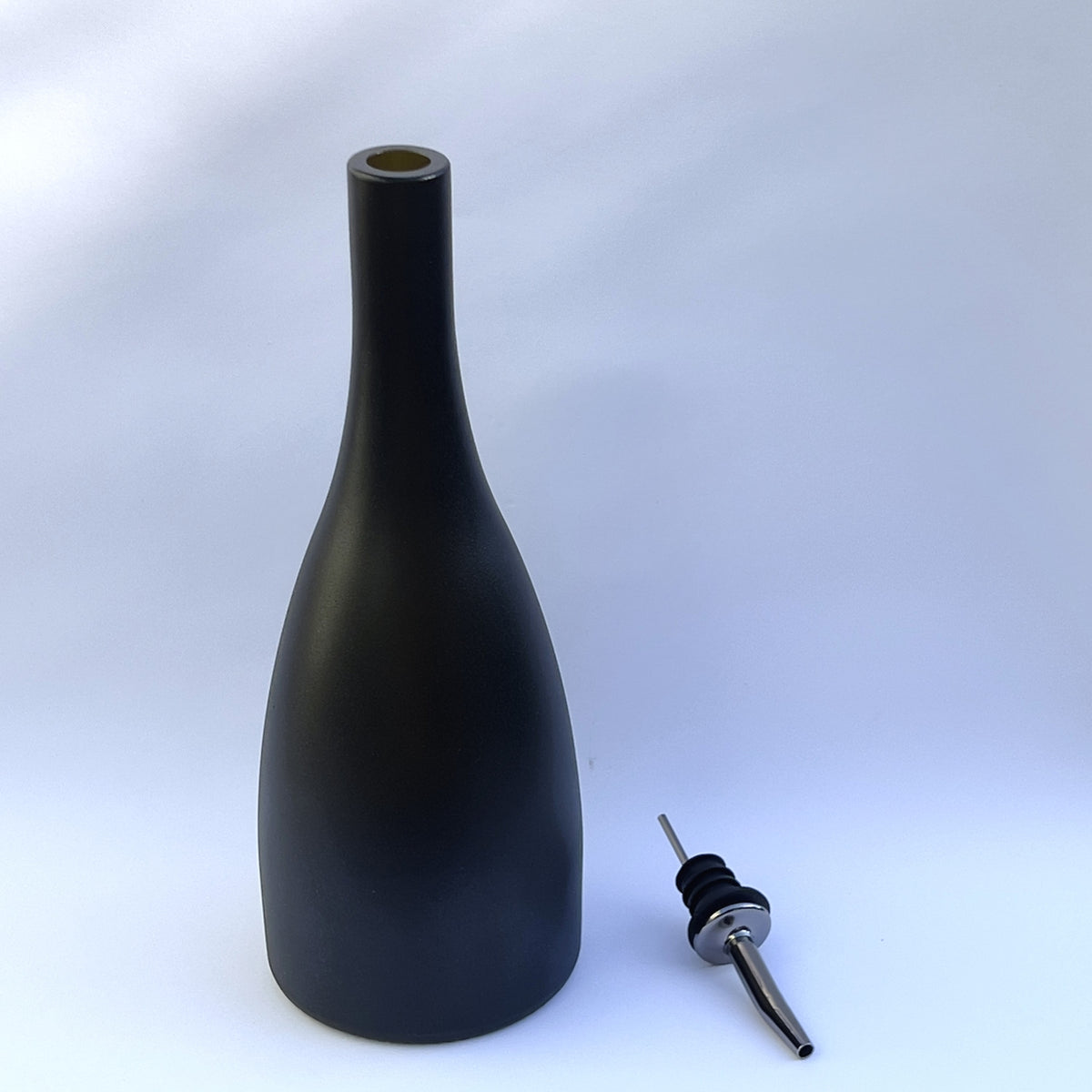 A matte black bottle-shaped pourer with a narrow neck and spout, shown next to a metal pour spout on a light gray background.